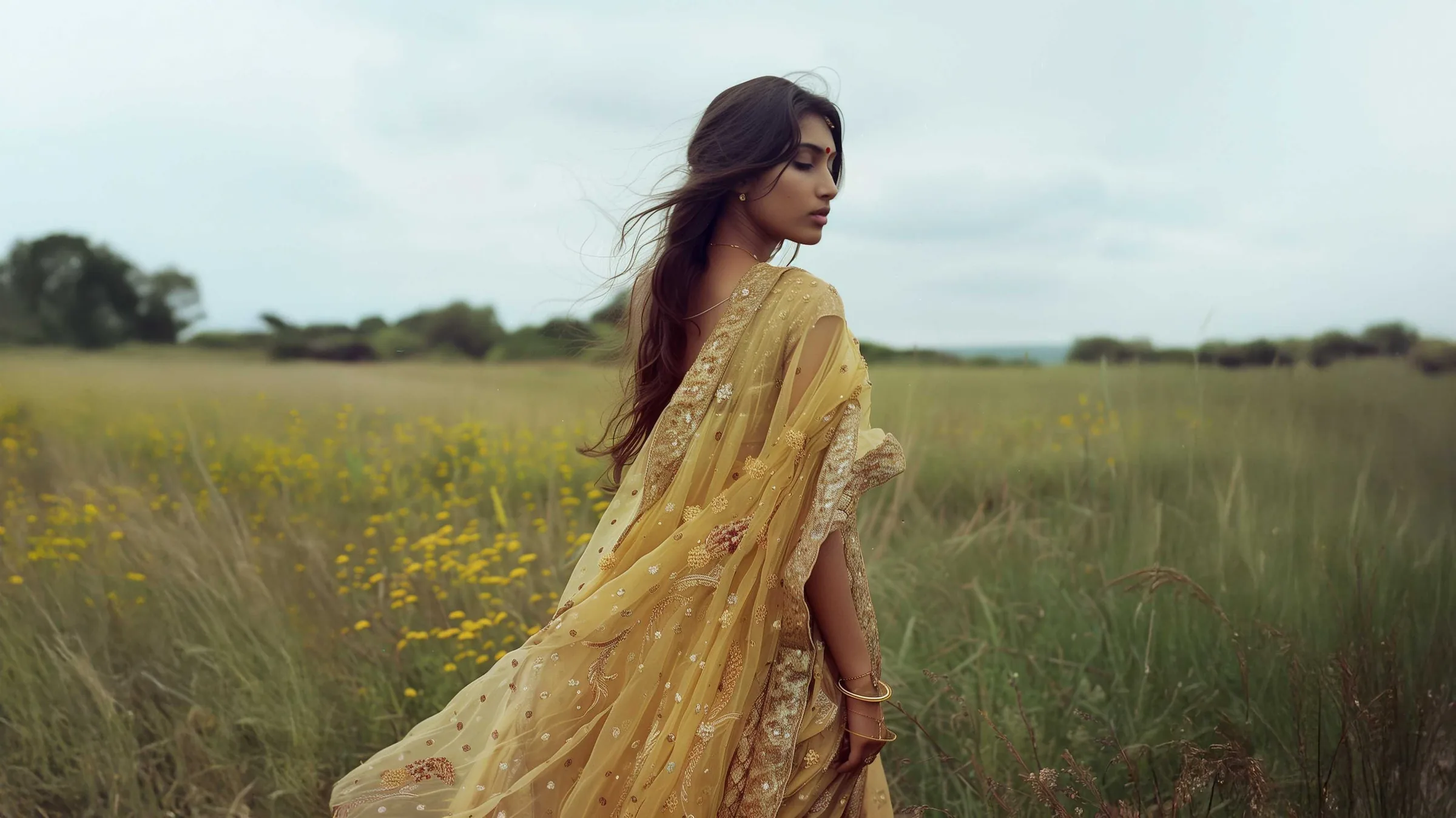A woman in a pale gold embellished saree standing in a field