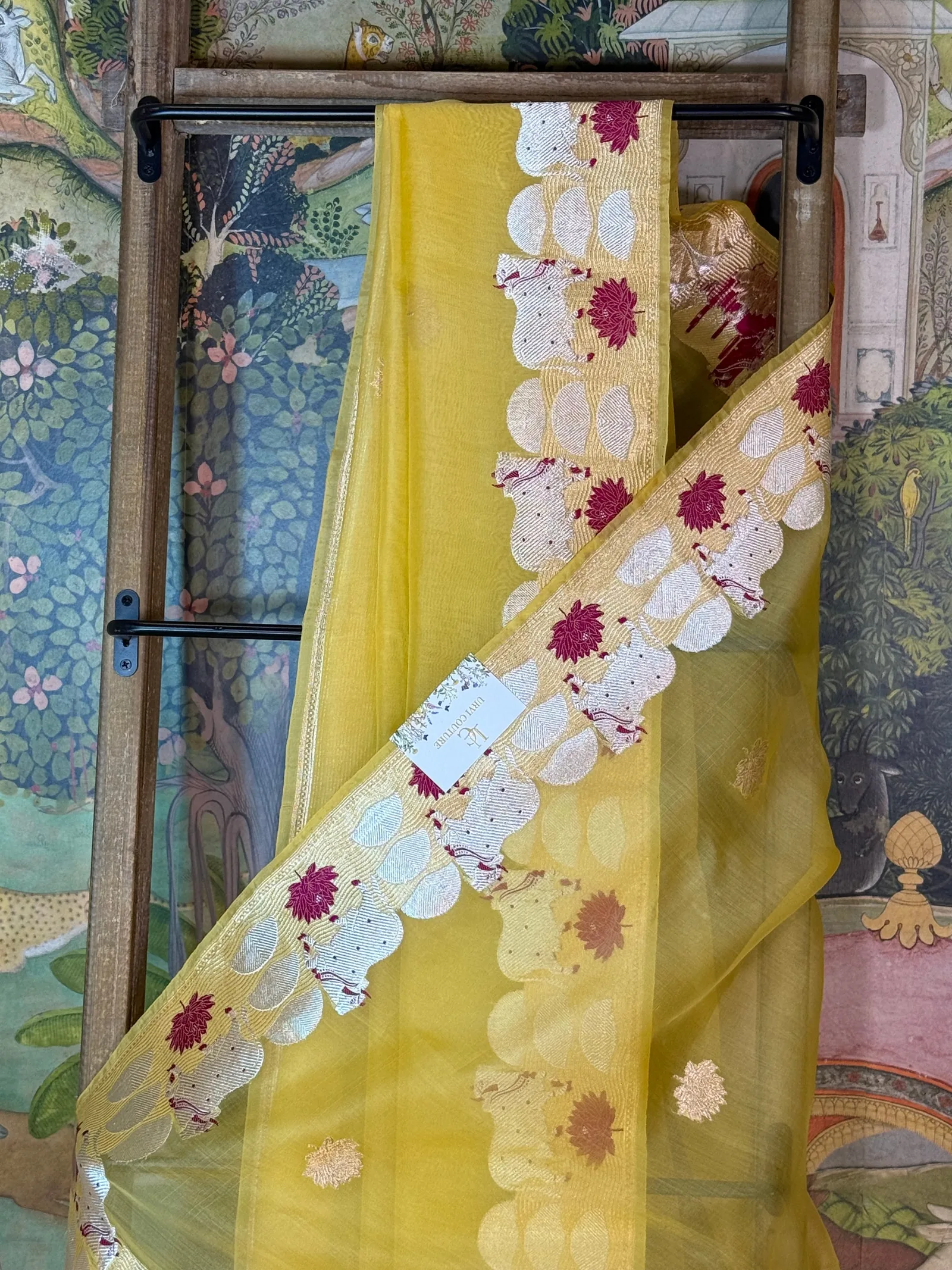 Benares Kora saree in yellow silk with a woven gold and maroon lotus border, draped over a wooden rack